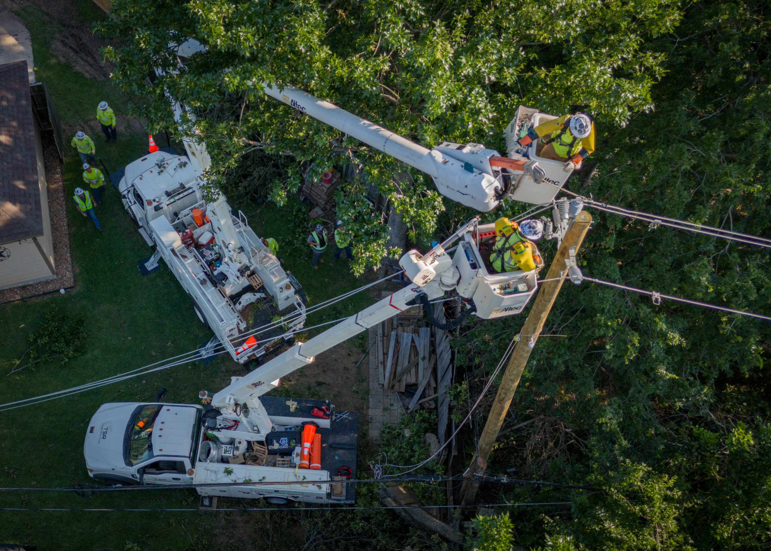 Drone photo of utility line workers in bucket trucks repairing power lines on a wooden utility pole in Houston.